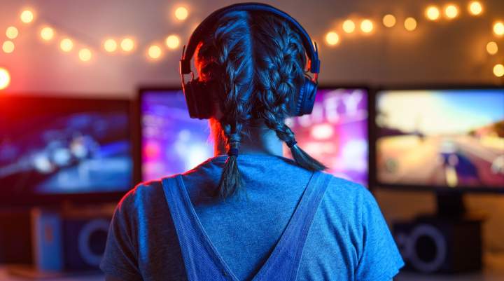 A view of the back of a woman gaming with desktop monitors in front of her.